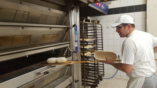 Mitarbeiter schiebt Brotteig in den Ofen
